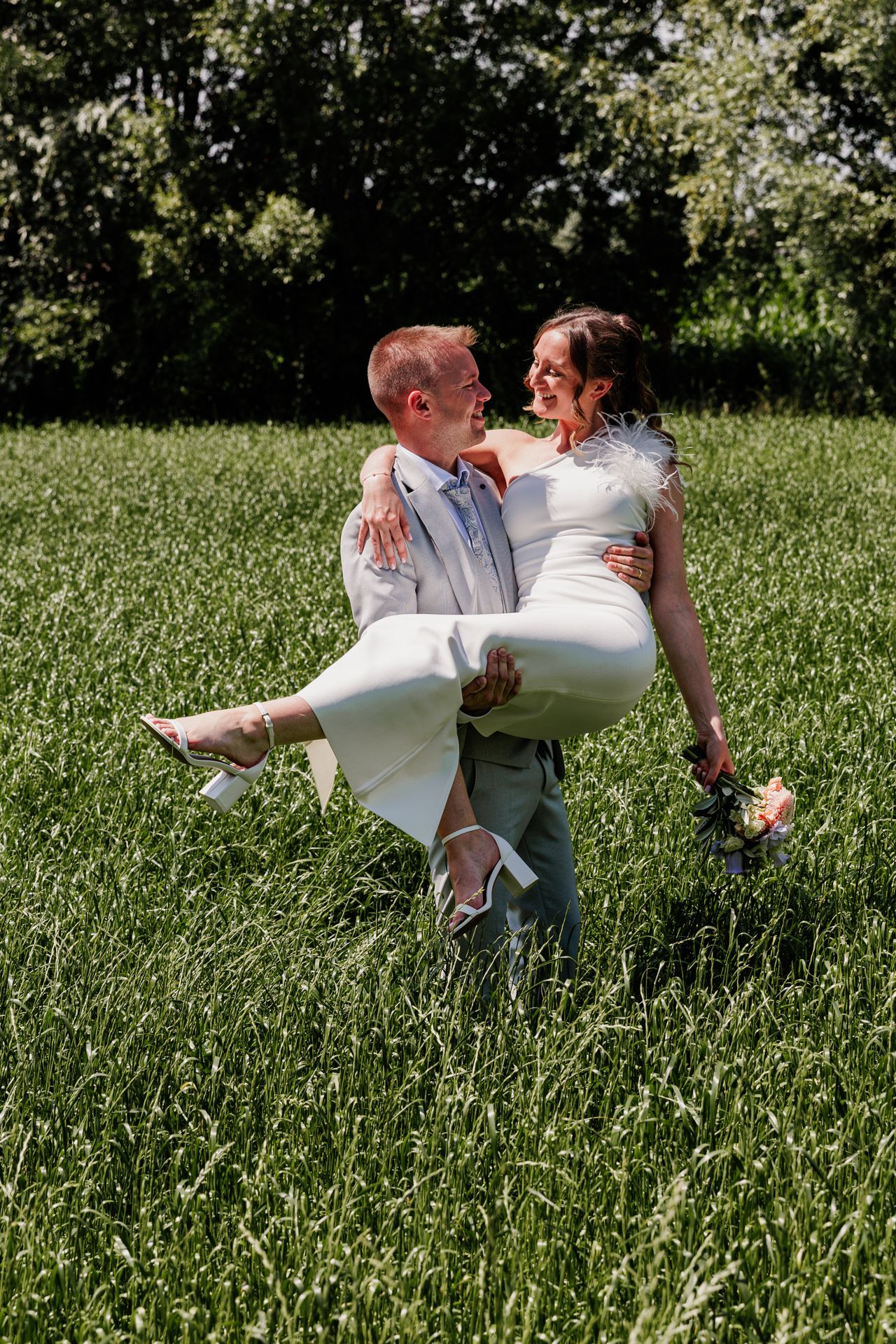 A man is lifting a woman in a white dress in a grassy field.