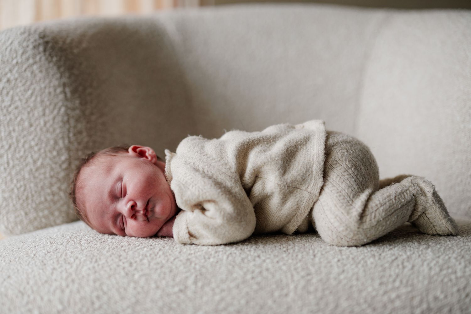 A newborn baby is sleeping peacefully wrapped in a soft, gray blanket on a couch.