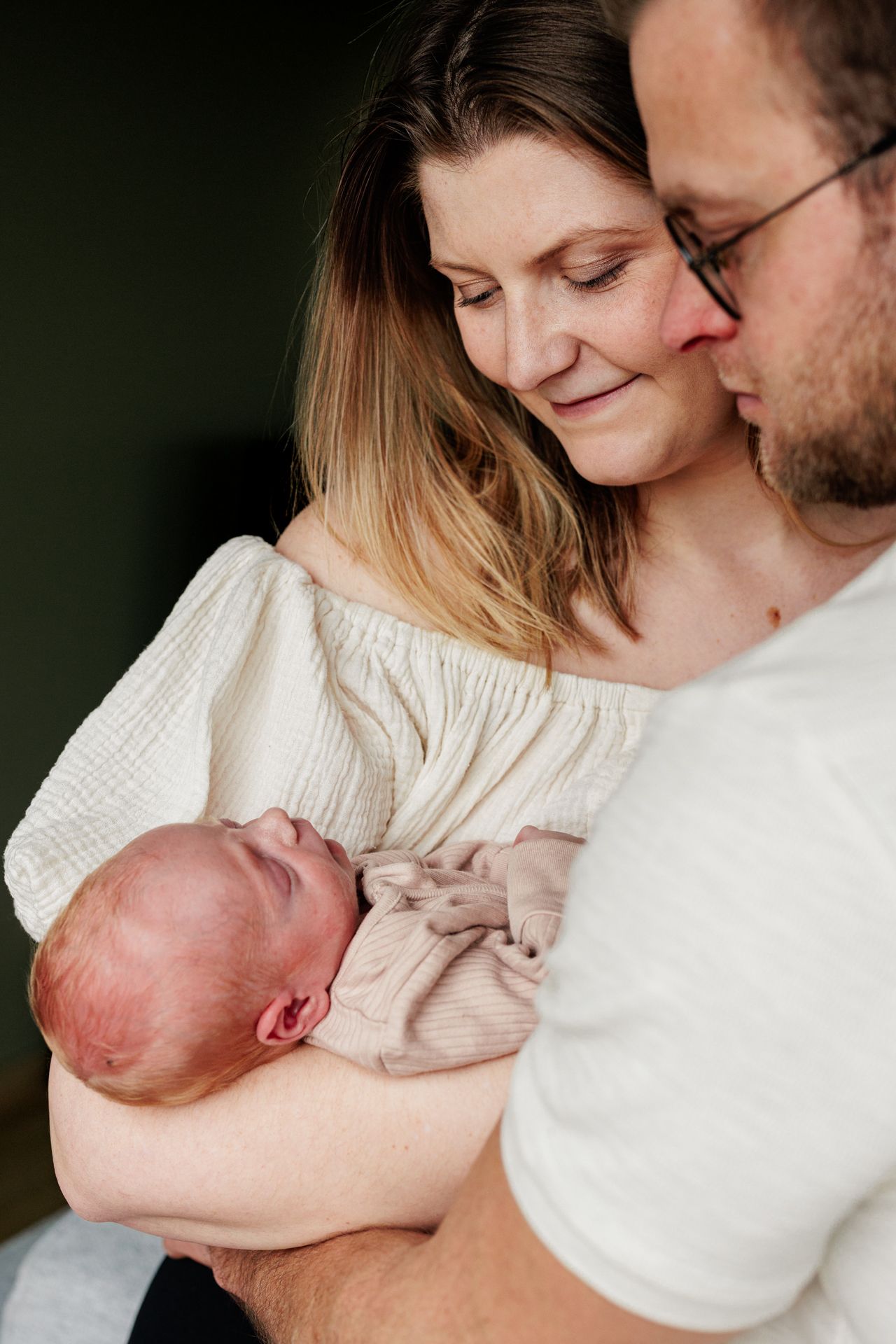 A young couple lovingly hold their newborn baby in a tender embrace.