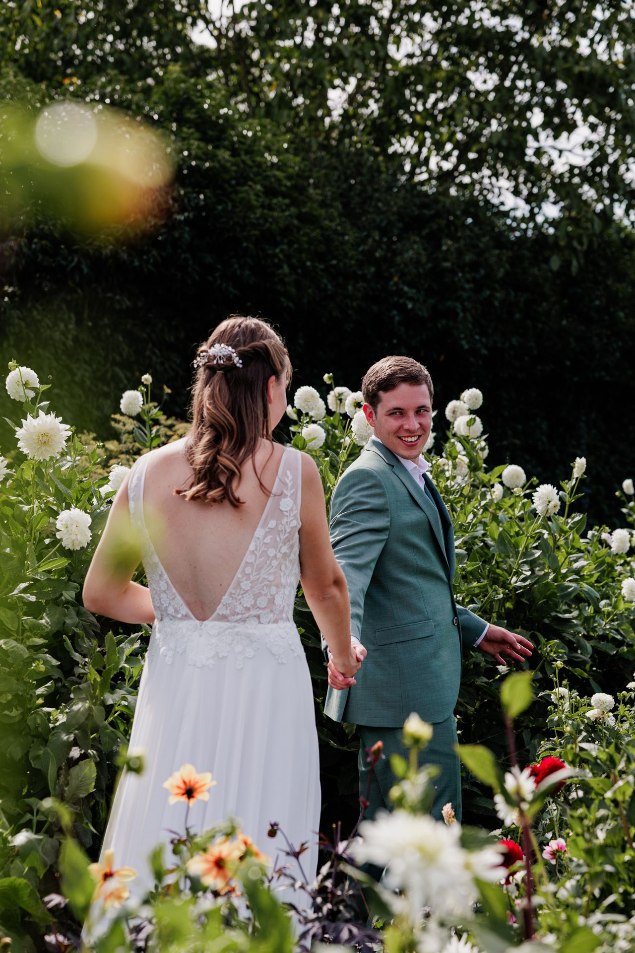 A bride and groom stand in a garden surrounded by flowers on their wedding day.