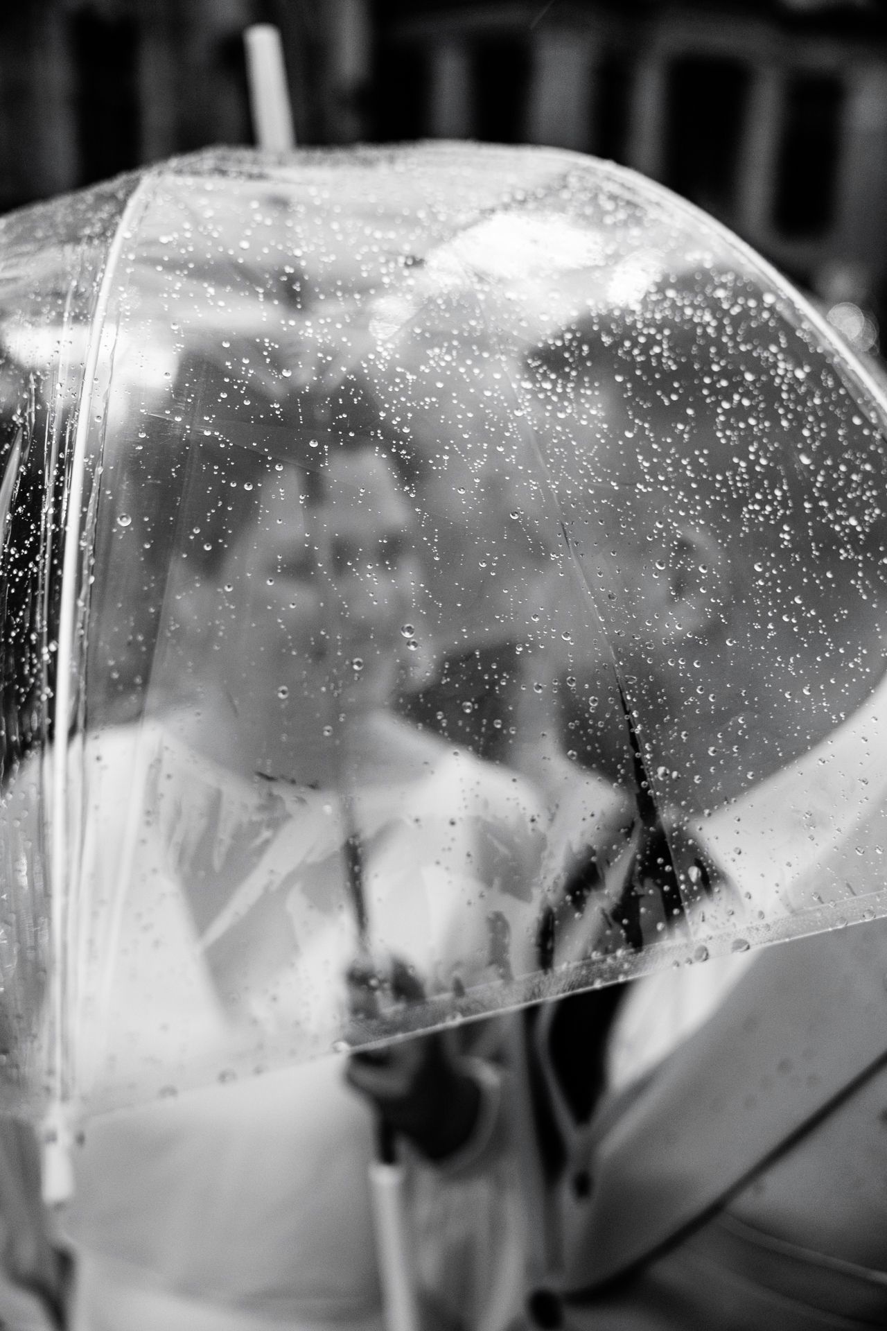 A black and white image of a person holding a transparent umbrella with water droplets visible on the surface.
