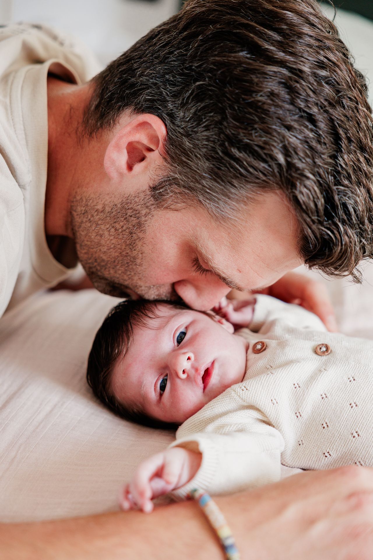 A loving father gently kisses his newborn baby on the forehead while the infant gazes upward peacefully.