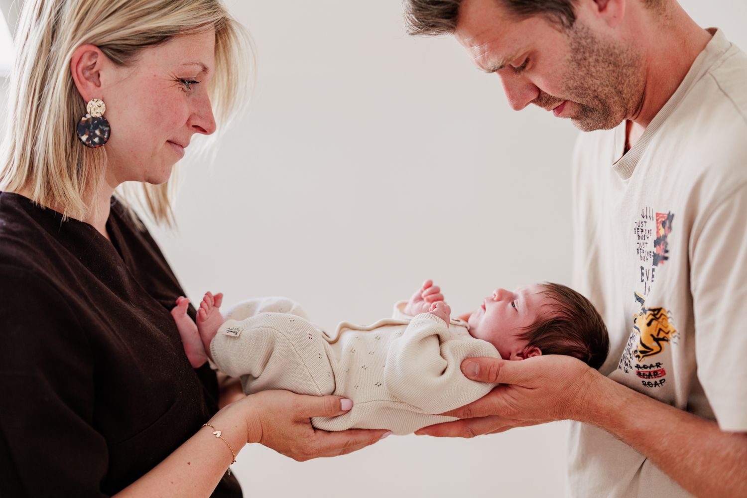 New parents lovingly cradle their swaddled newborn baby together in a tender family portrait.