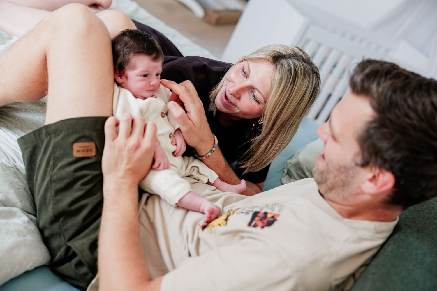 New parents lovingly admire their newborn baby together on a couch in a tender family moment.