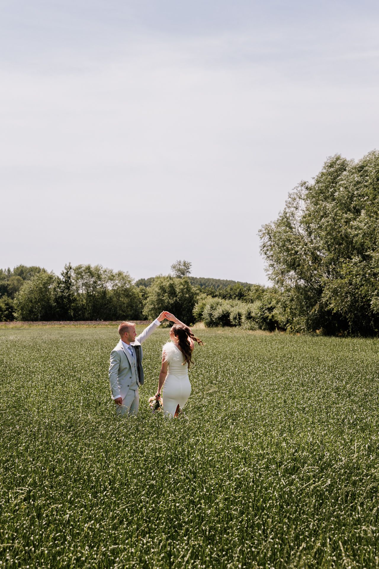 A man and woman walk hand-in-hand through a lush green field with trees in the background.