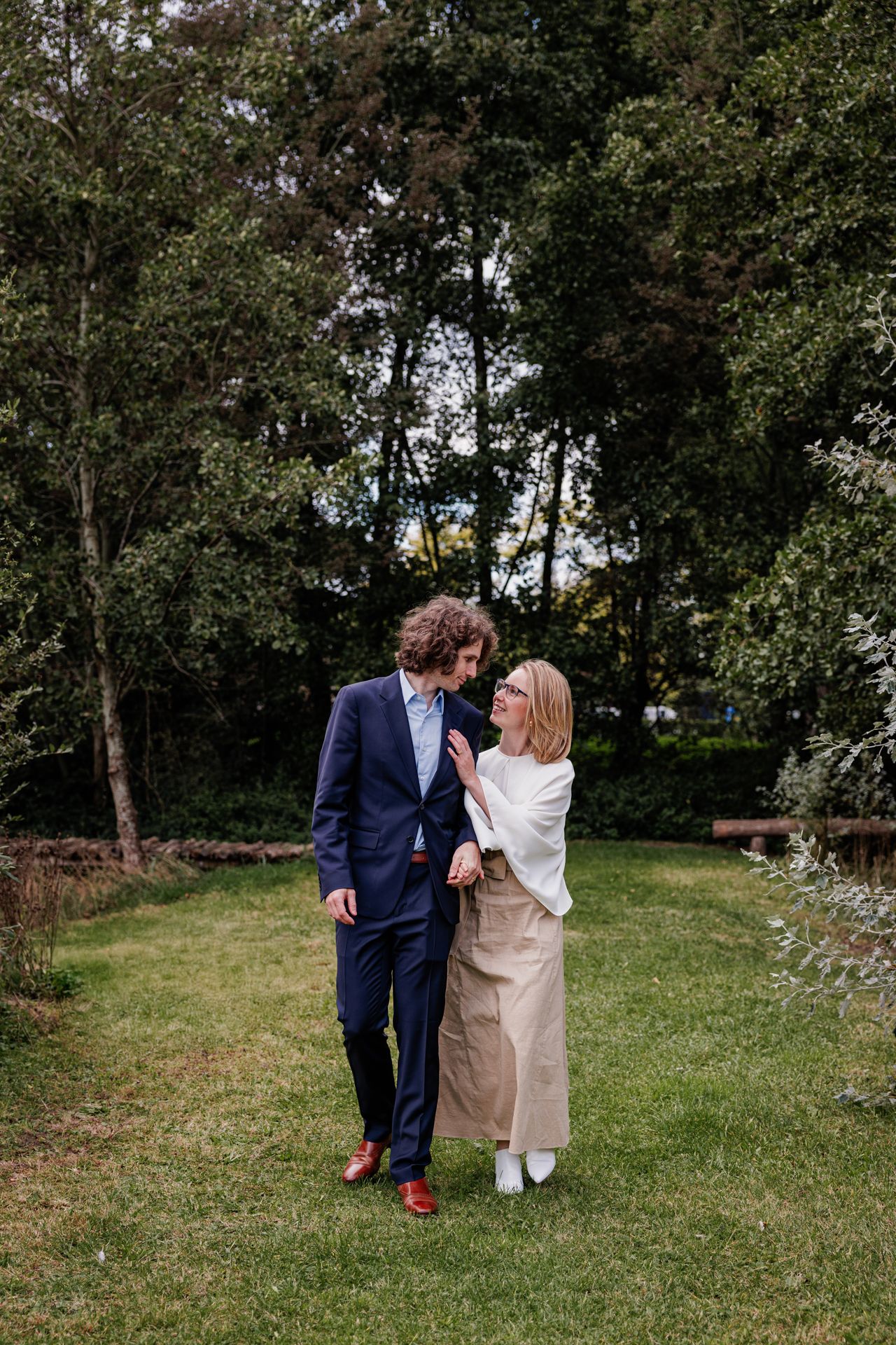 A couple standing together in a lush, wooded garden.