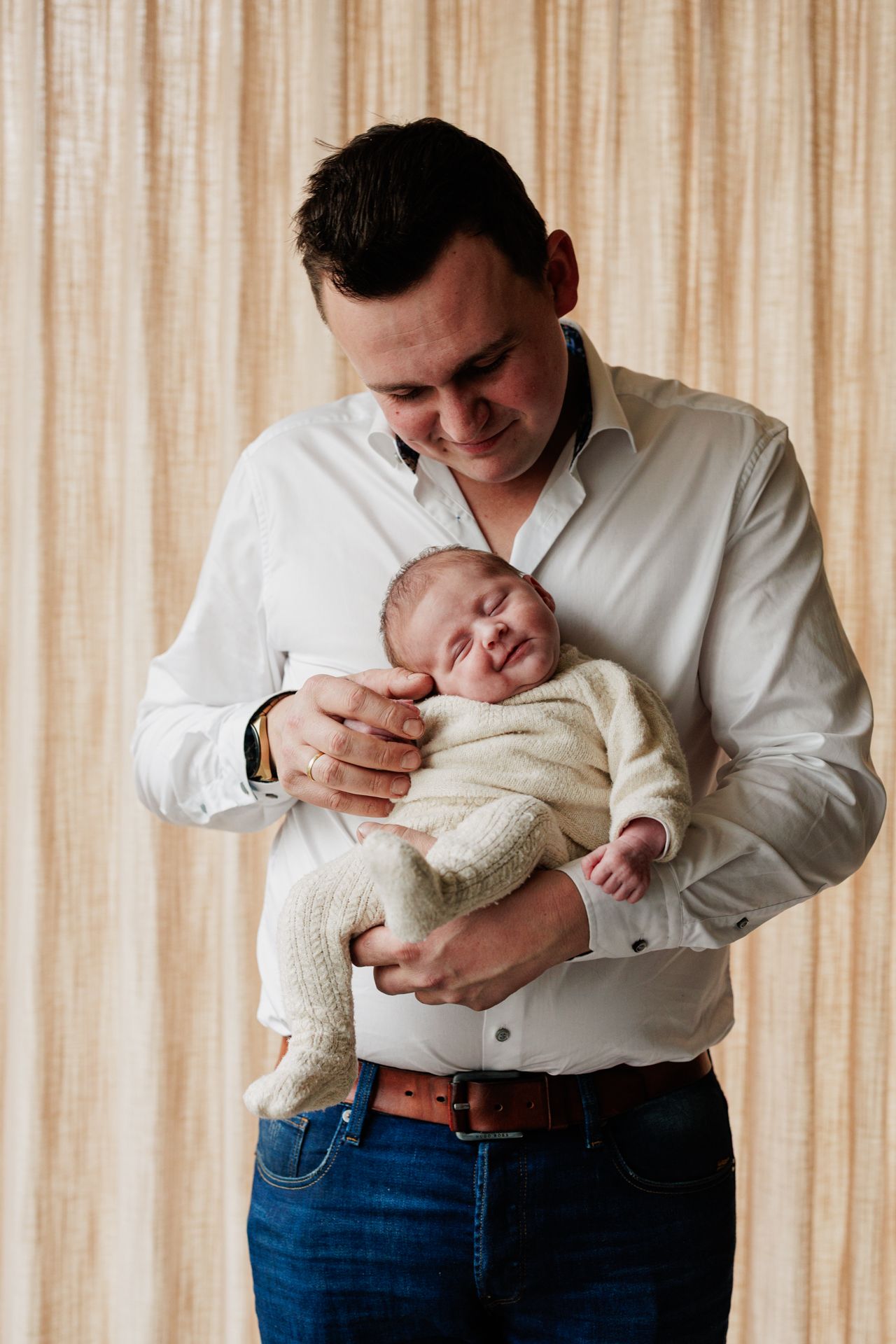 A man in a white shirt is holding a sleeping newborn baby in his arms.