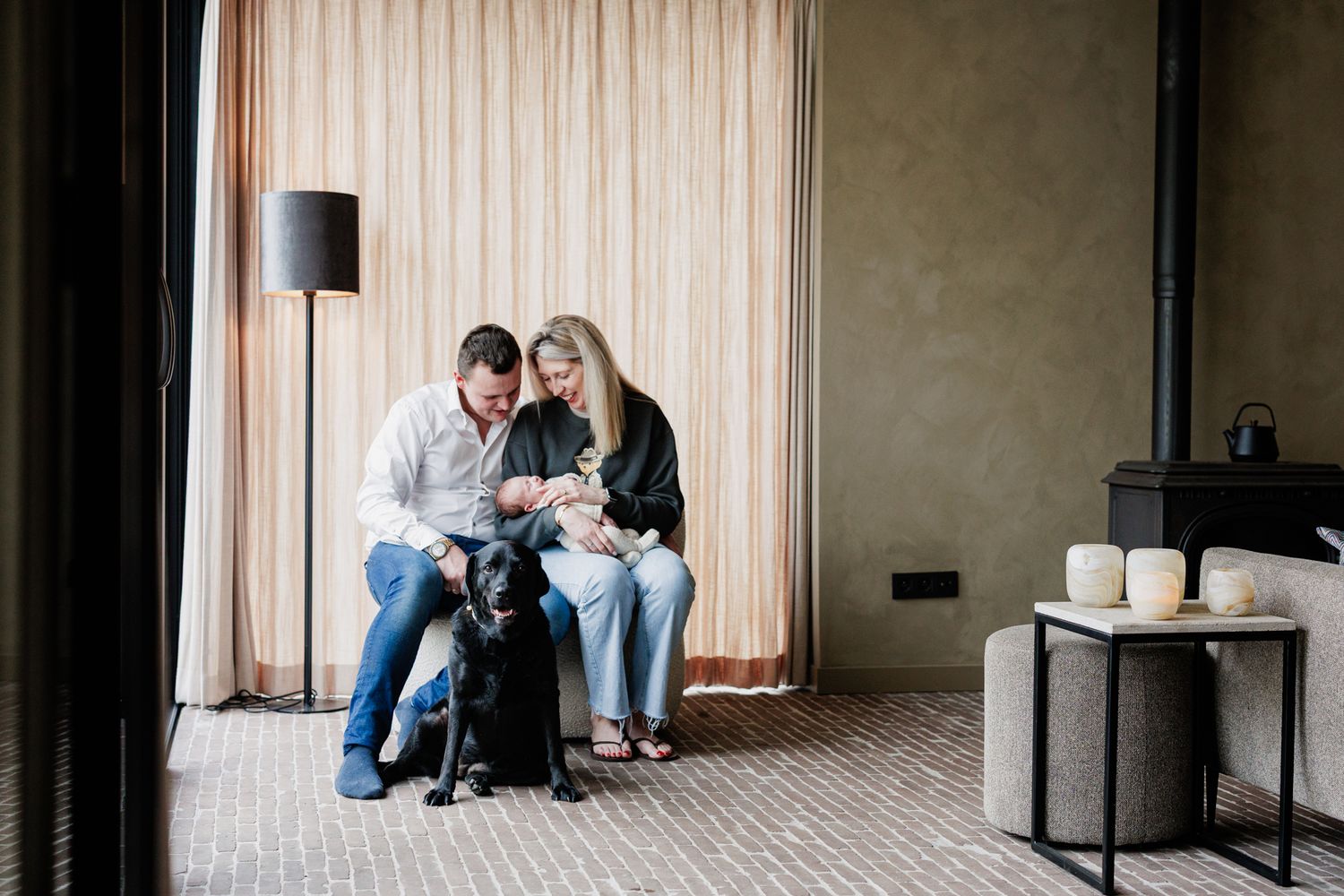 A couple sitting on a couch with their dog, in a cozy living room setting.