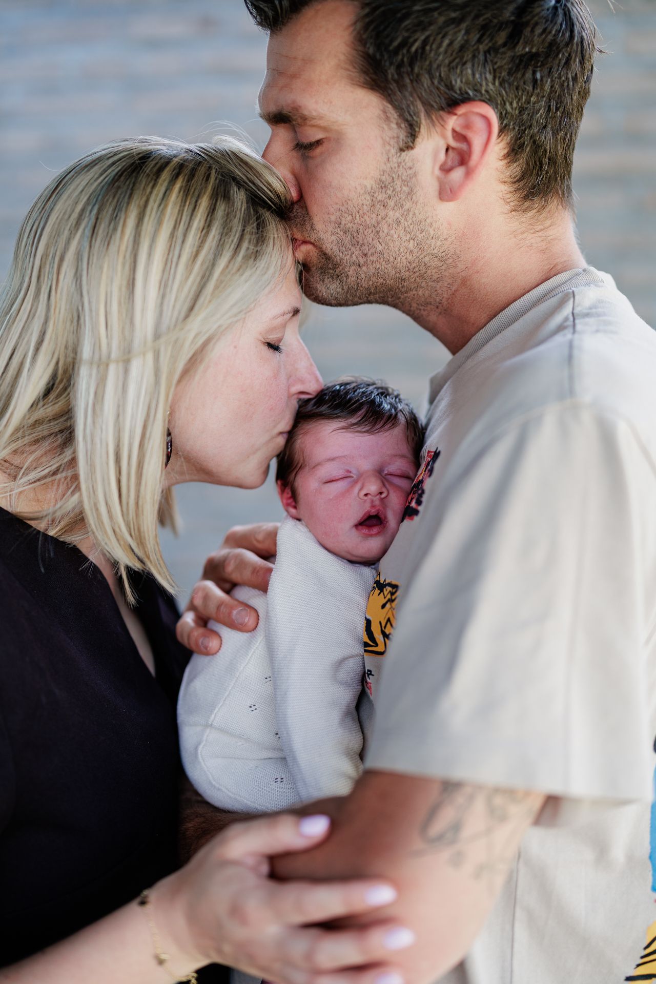 Two parents kissing their newborn baby, a tender family moment captured in a heartwarming portrait photo.