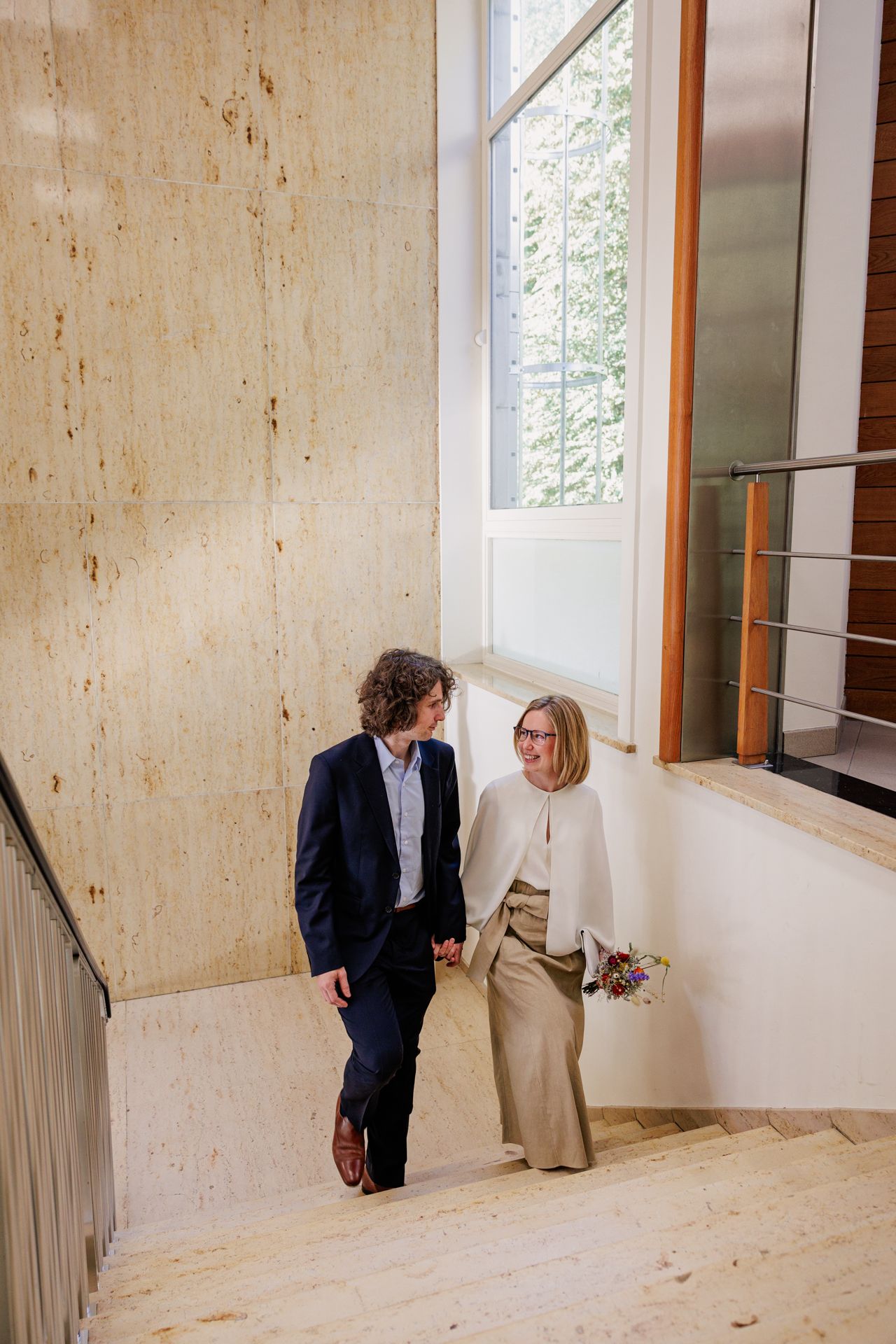 Two people, a man and a woman, are walking up a set of wooden stairs in an indoor setting.