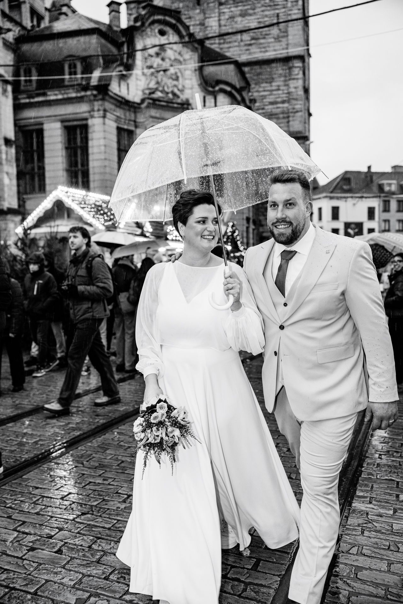 Zwart wit foto van bruid en bruidegom die samen wandelen in de regen, in het centrum van Gent met een paraplu in de hand.