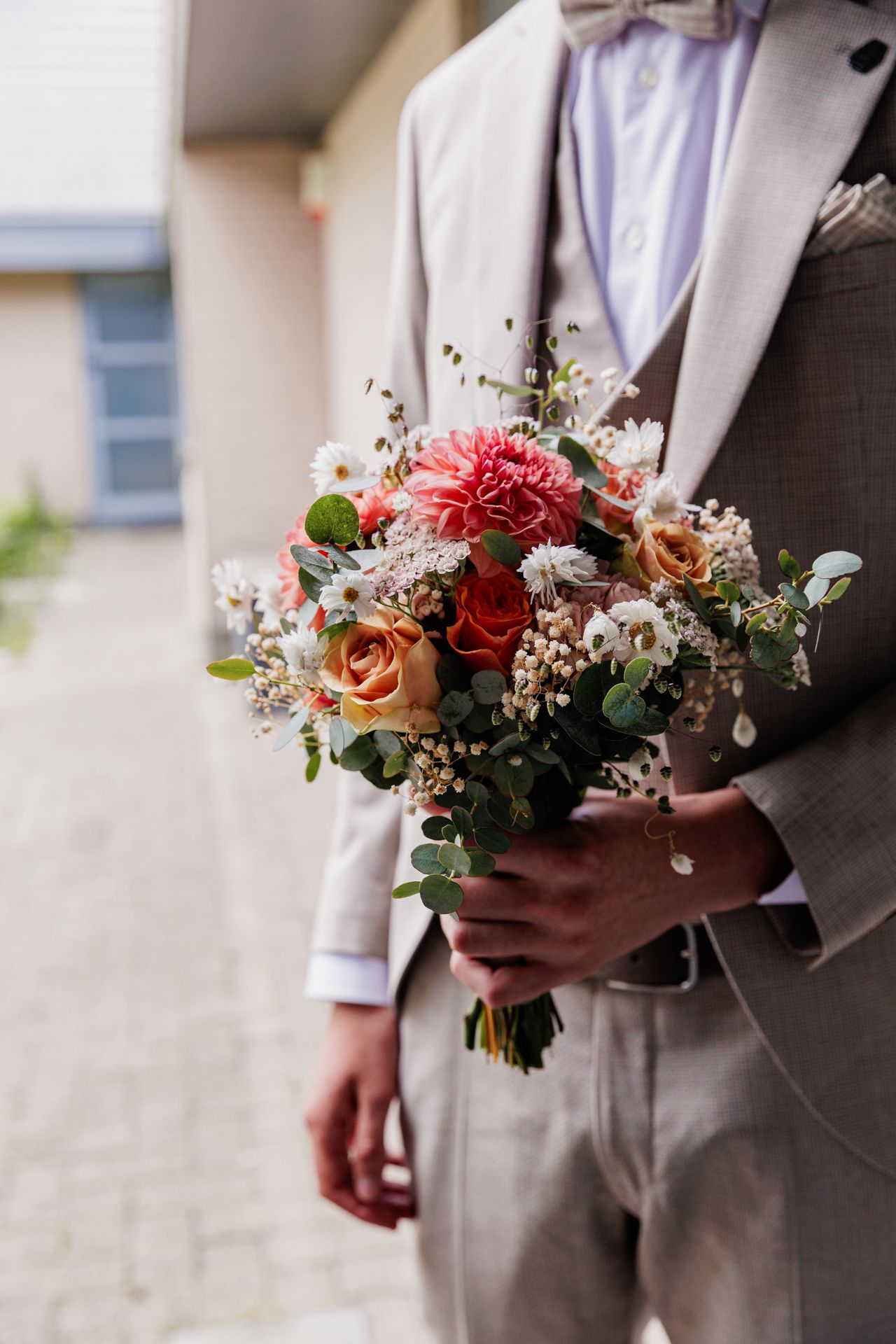 A bouquet of colorful flowers, including red and pink flowers, held by a person wearing a gray suit.