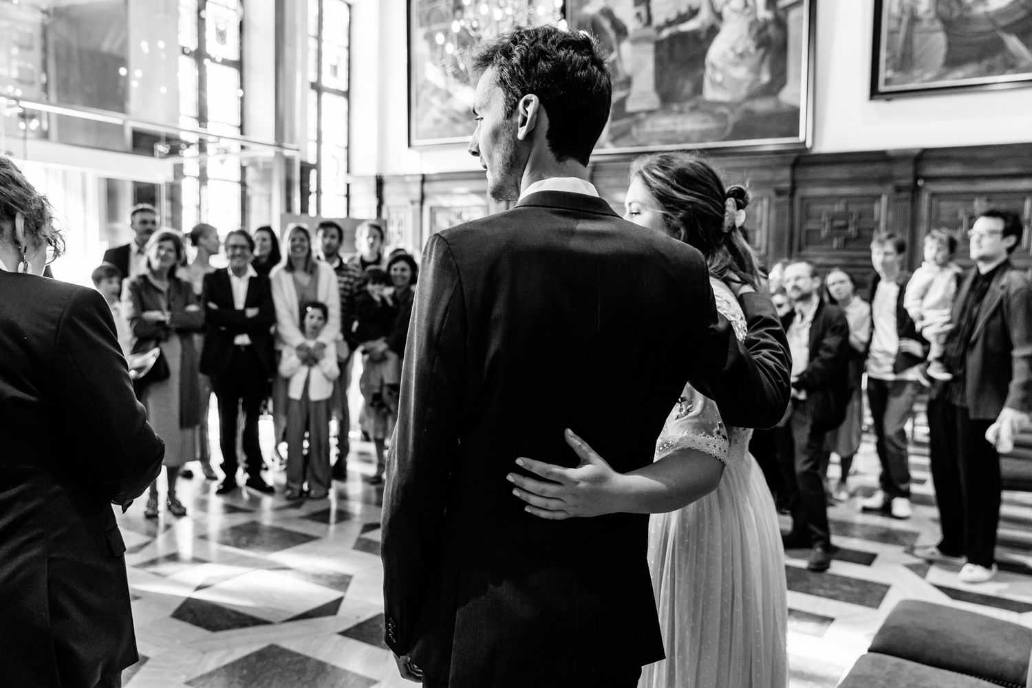A black and white image of a bride and groom standing together in a crowded church or venue, surrounded by guests.