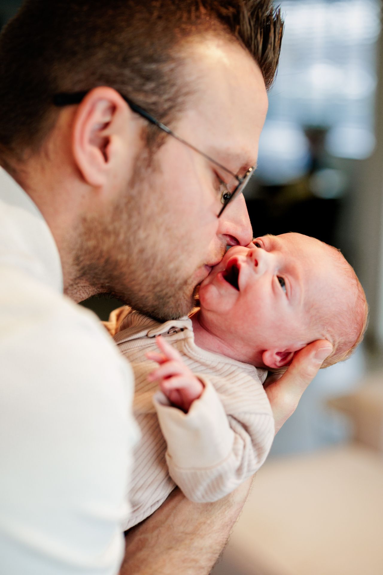 A man gently holding and kissing a newborn baby in his arms.