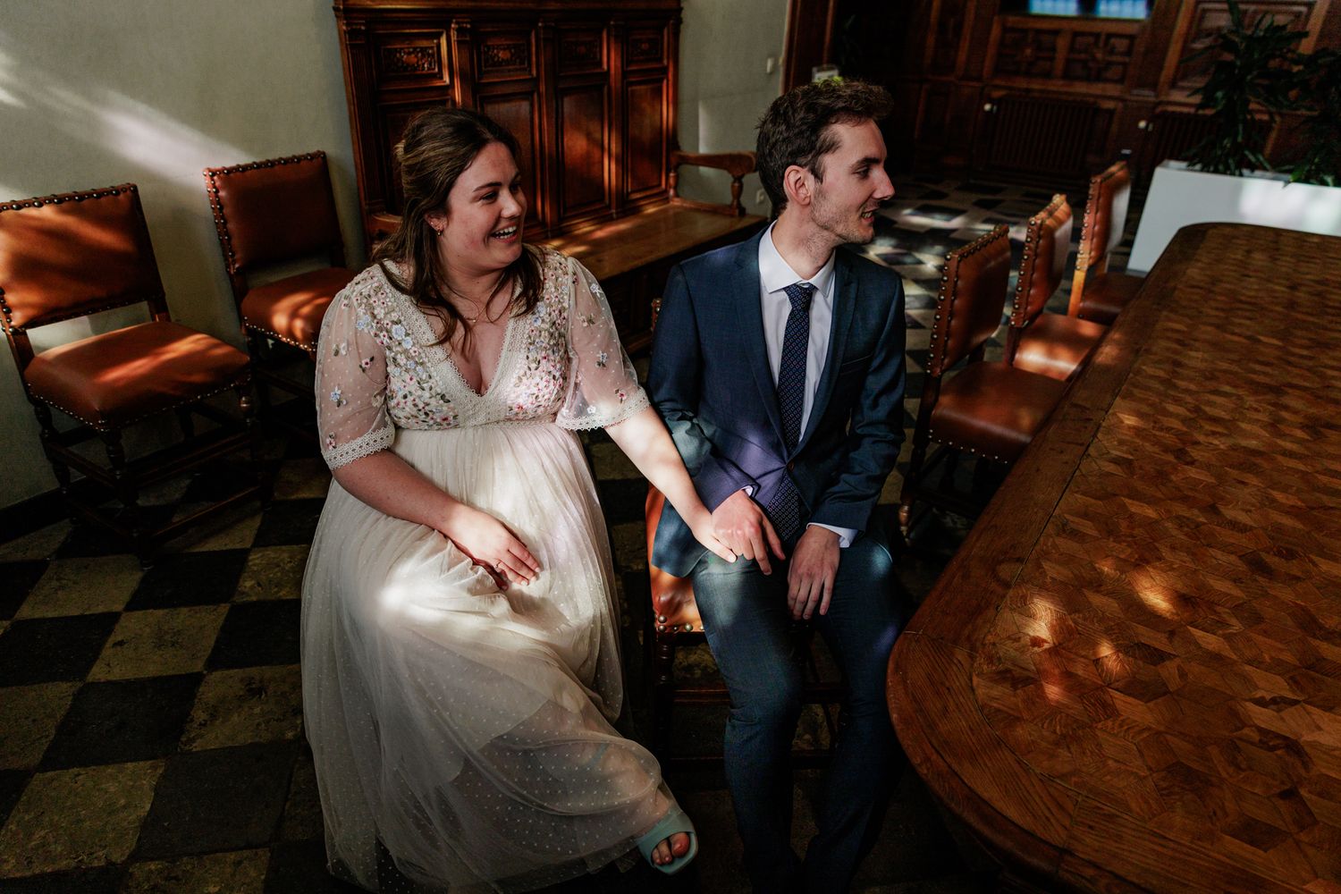 A couple dressed in formal attire stand together in a room with ornate furniture.