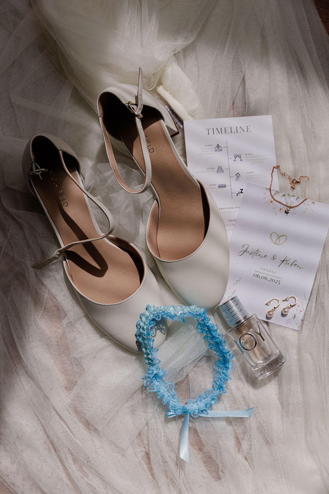The image shows a pair of white bridal shoes, a timeline, and a blue bracelet on a white tulle background.