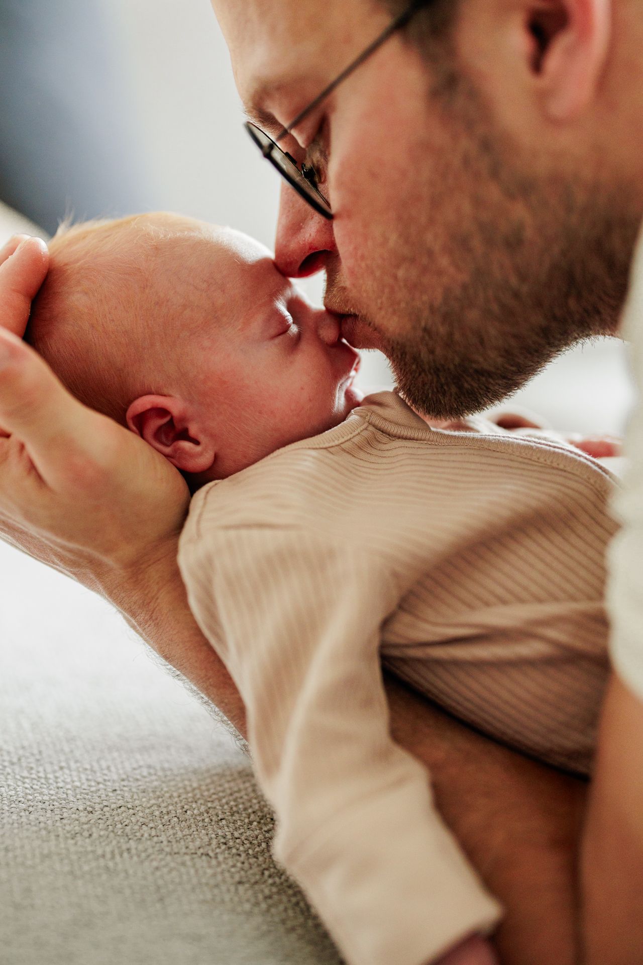 A close-up image of a man gently holding and kissing a newborn baby in his arms.