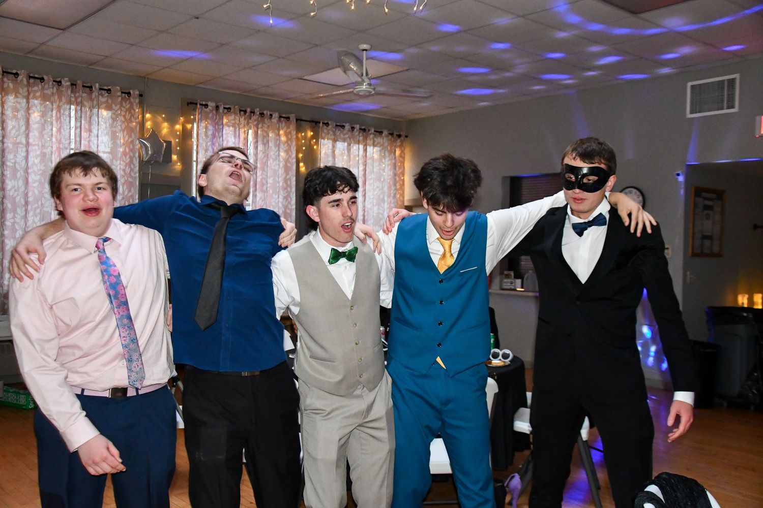 Group of five young people posing together at a dance party with disco lights on the ceiling.