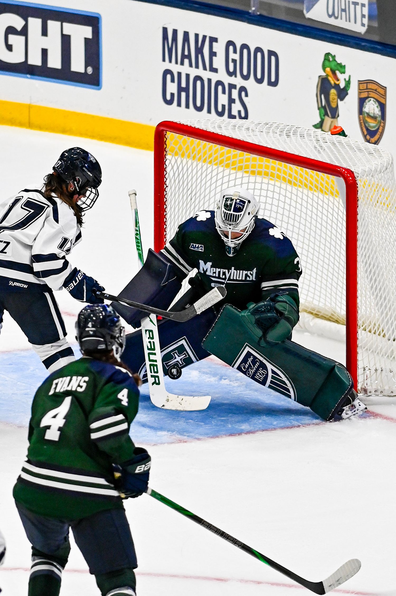 Ice hockey players in green and white jerseys compete for the puck during an intense game at an indoor rink.
