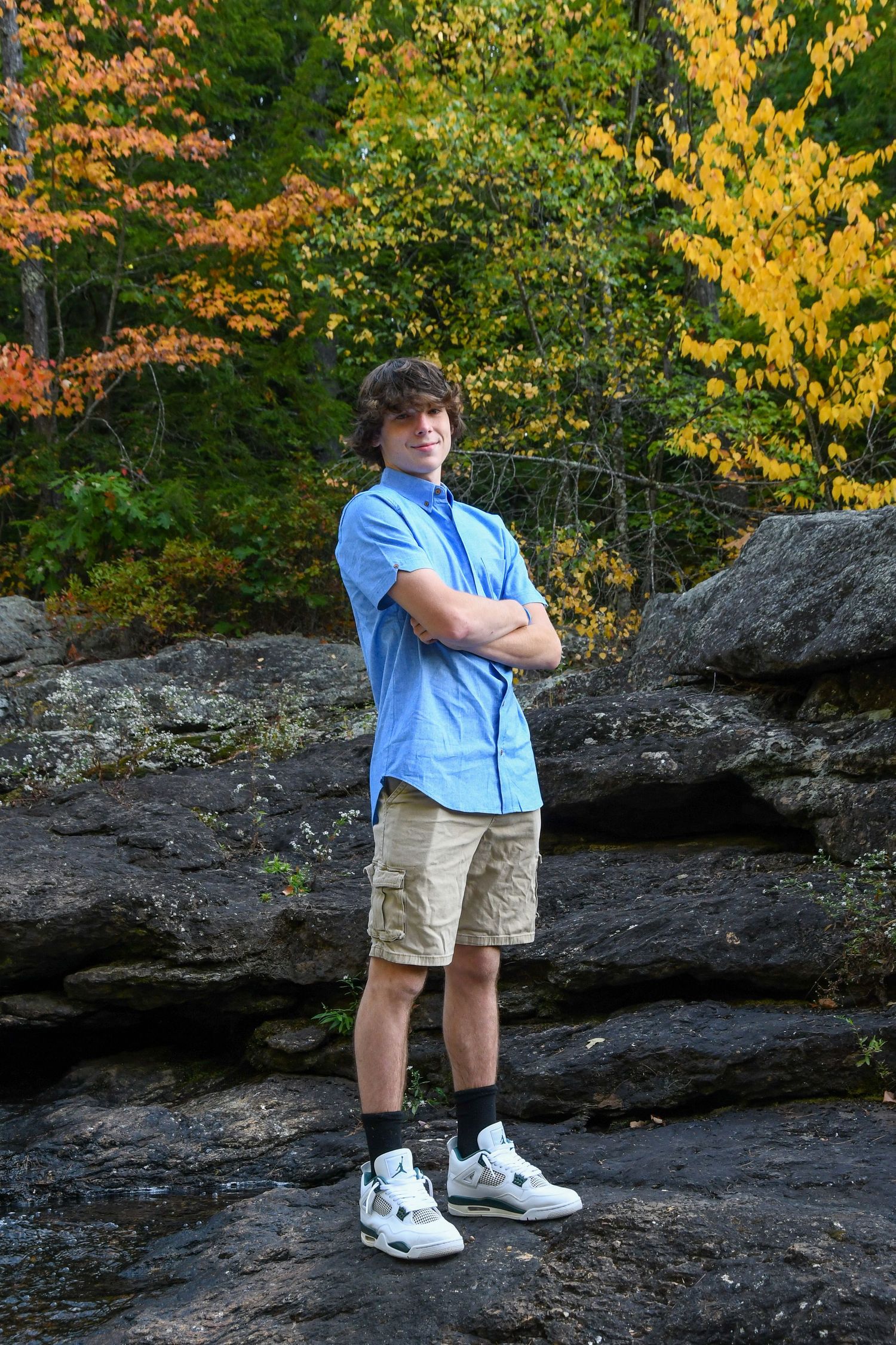 Person poses confidently on rocky ledge wearing blue shirt and white sneakers.