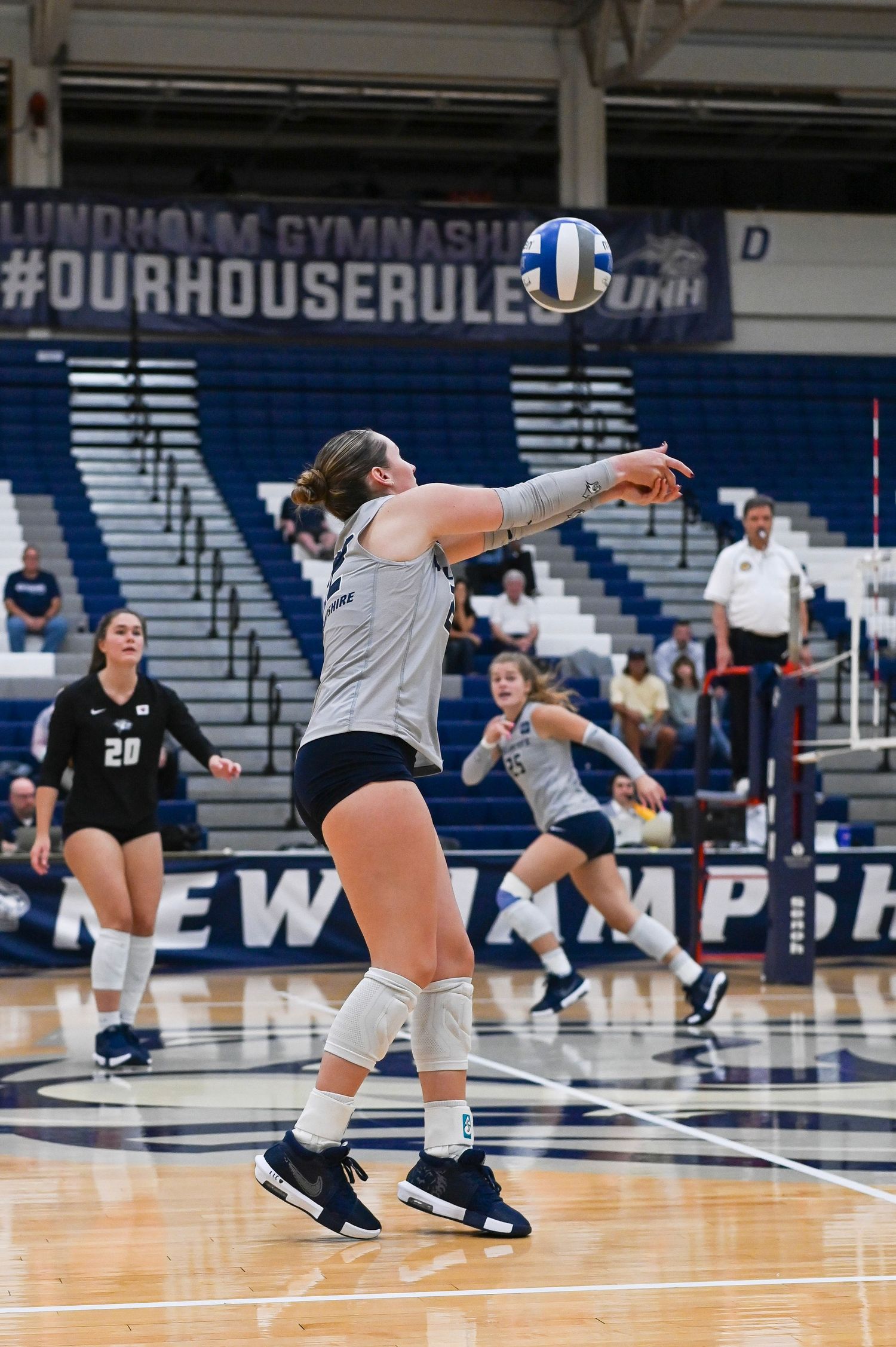 Volleyball players diving and reaching for the ball during an intense indoor match at Lundholm Gymnasium.