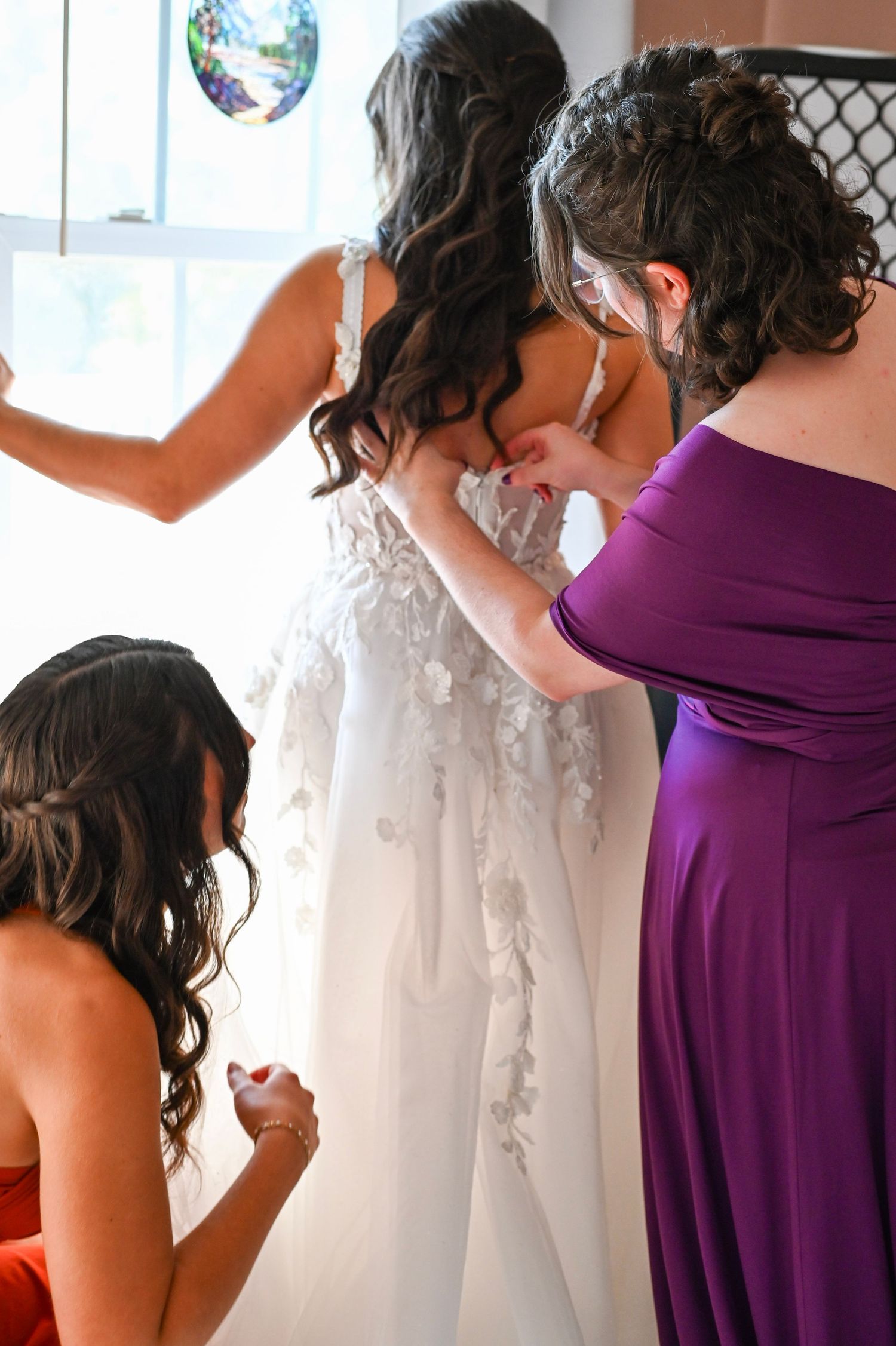 A person in a purple bridesmaid dress examines white wedding gowns hanging on a rack in a bridal boutique.