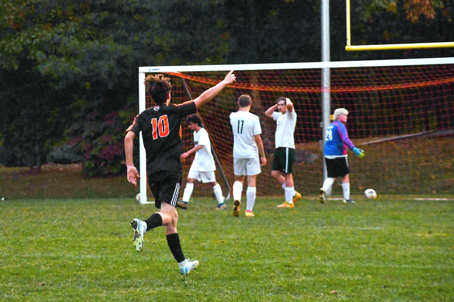Soccer player in orange jersey preparing to kick ball on field with goal in background.