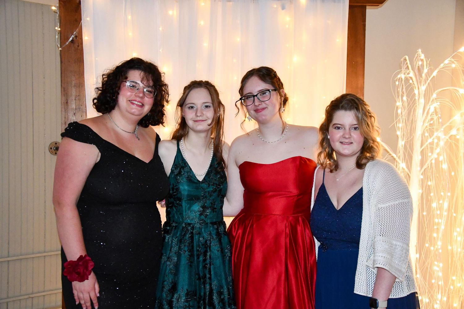 Four people in formal attire pose together at an event with decorative lights and curtains in the background.