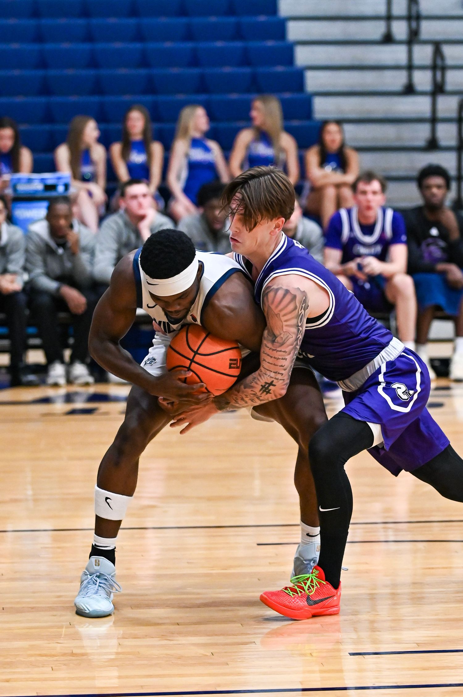 Two basketball players battle for possession of the ball during an intense game on a hardwood court.