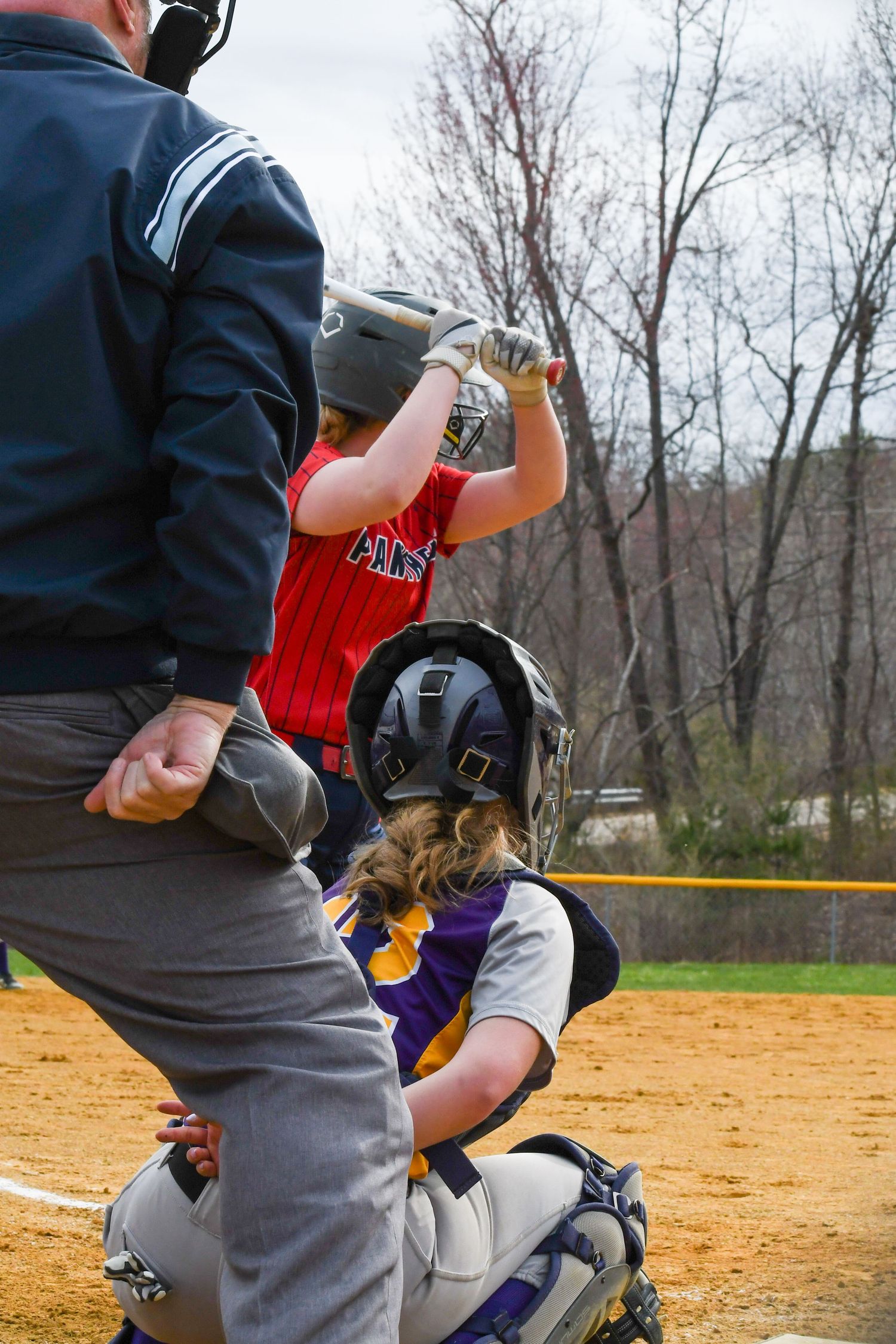 Baseball catcher crouched behind home plate in catching stance during game on dirt infield.