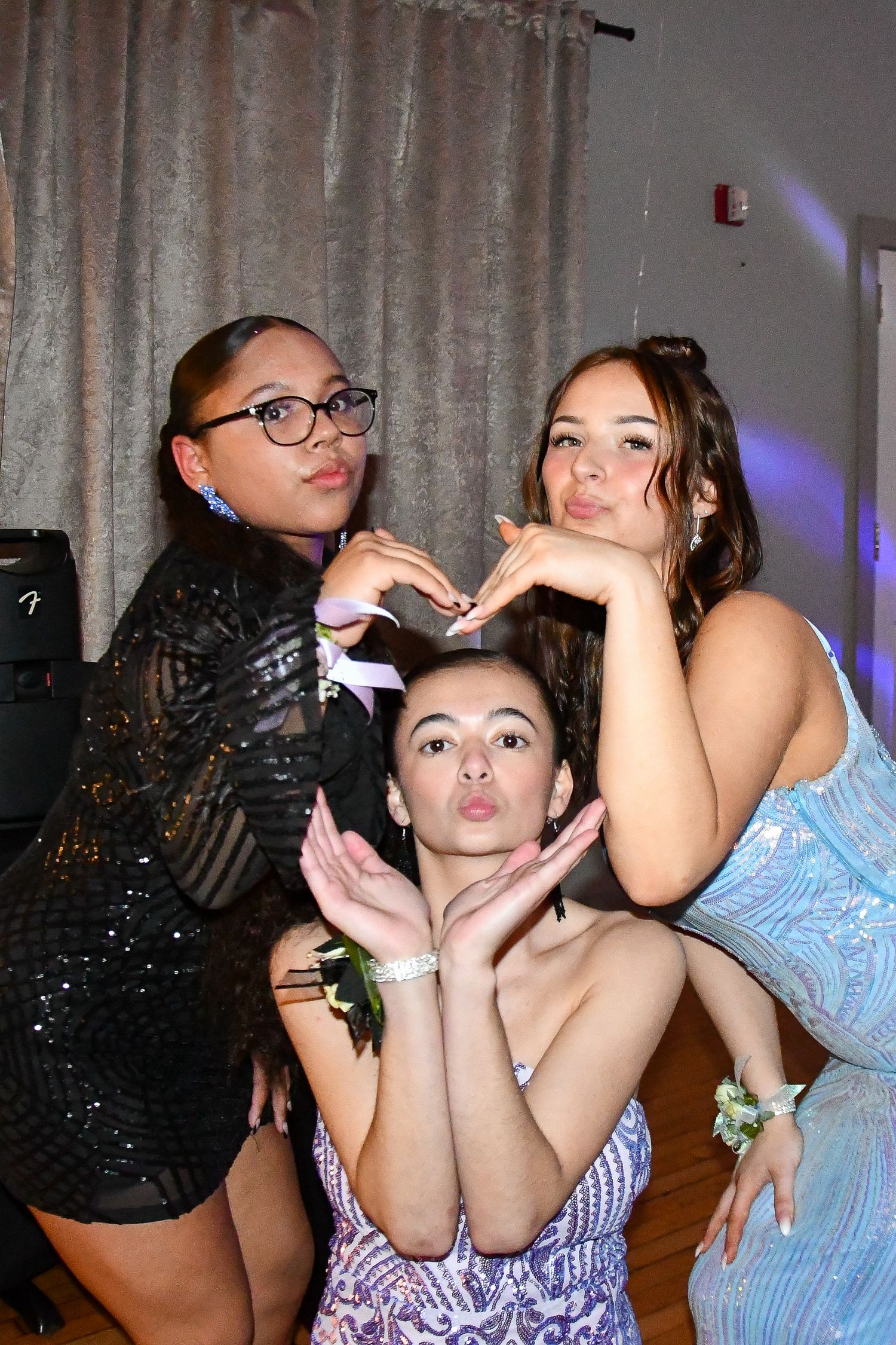 Friends pose playfully at a formal event wearing elegant dresses under party lights.