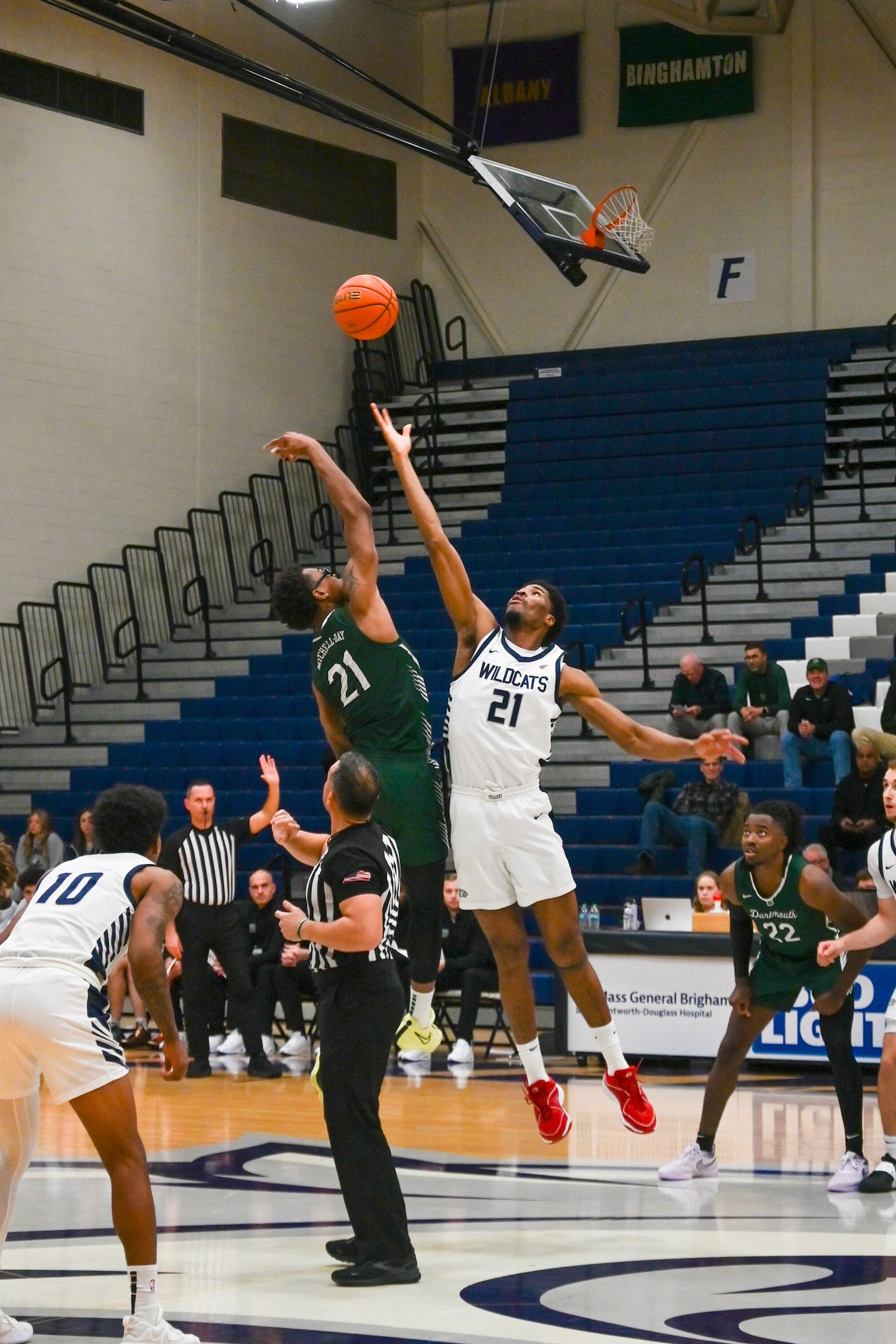 Basketball players jump high to compete for the ball during an intense game in a gymnasium.