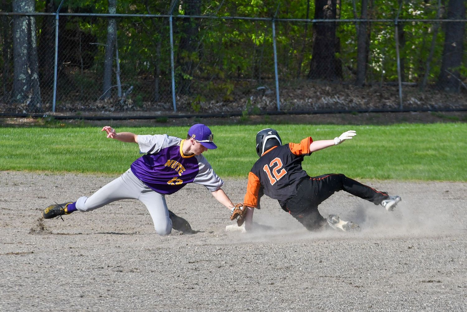 Baseball player in purple jersey attempts to tag out sliding opponent in black uniform during dramatic play at the base.