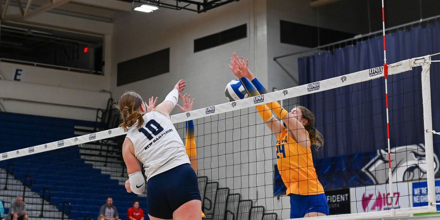Volleyball players leap to block a spike at the net during an intense indoor match.