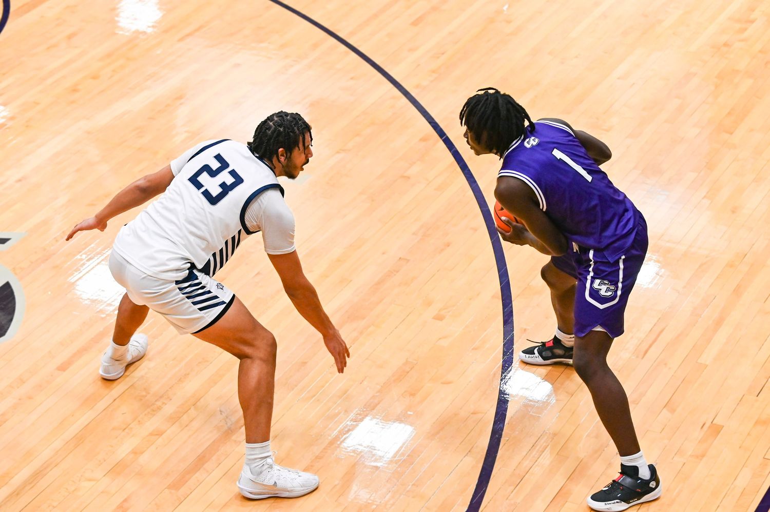 Basketball player dribbles low while driving past defender during competitive game on wooden court.
