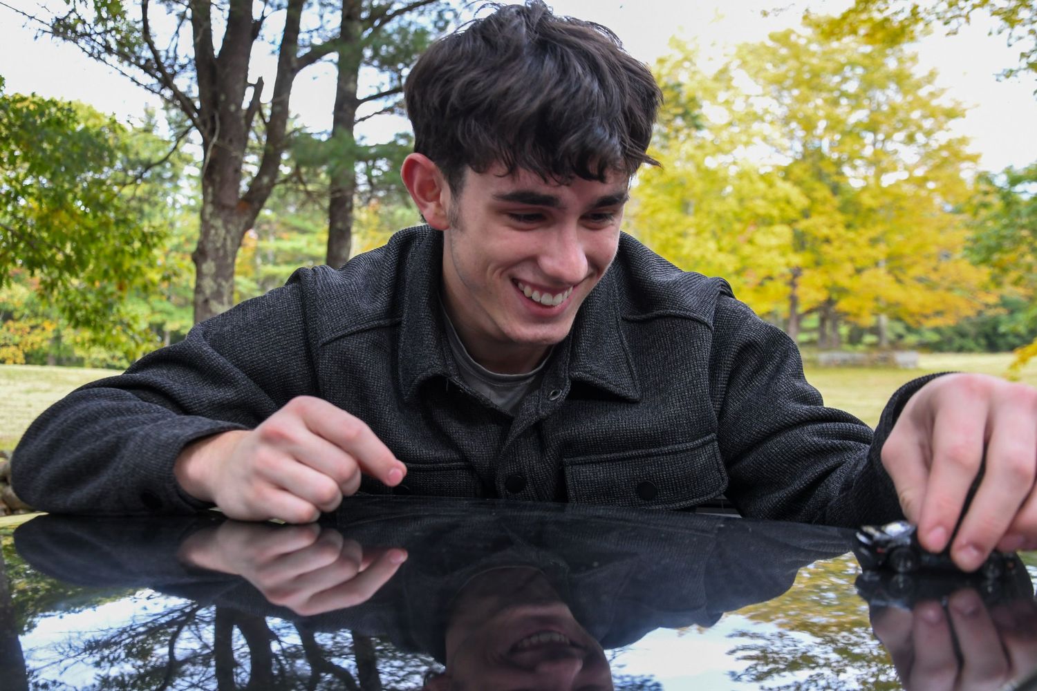 Person leaning over reflective surface outdoors with joyful expression.
