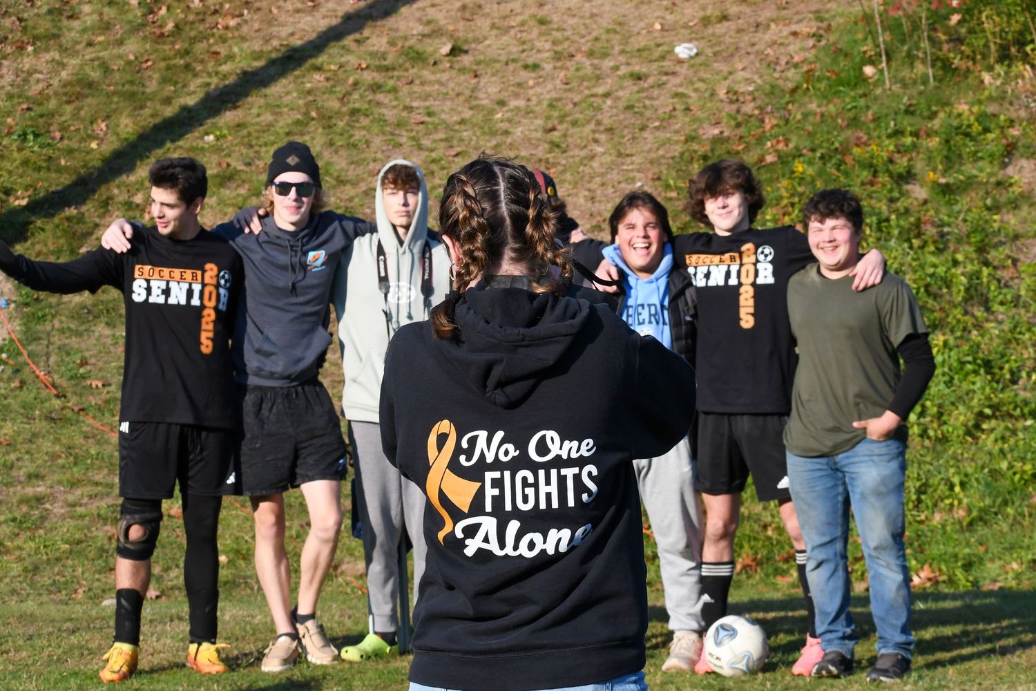 Group photo of people wearing casual clothes gathering outdoors on a grassy hill.