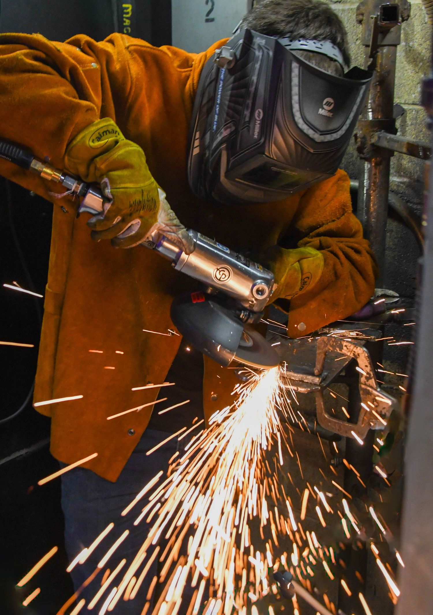 Welder in protective gear working with metal creating sparks.