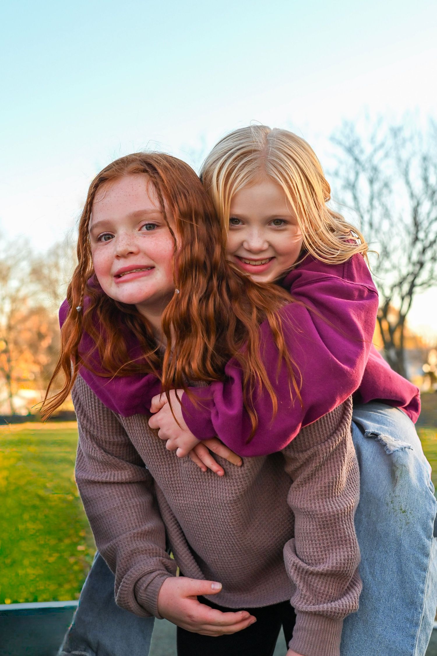 Two people playing and laughing together outdoors in a playful piggyback pose during golden hour.