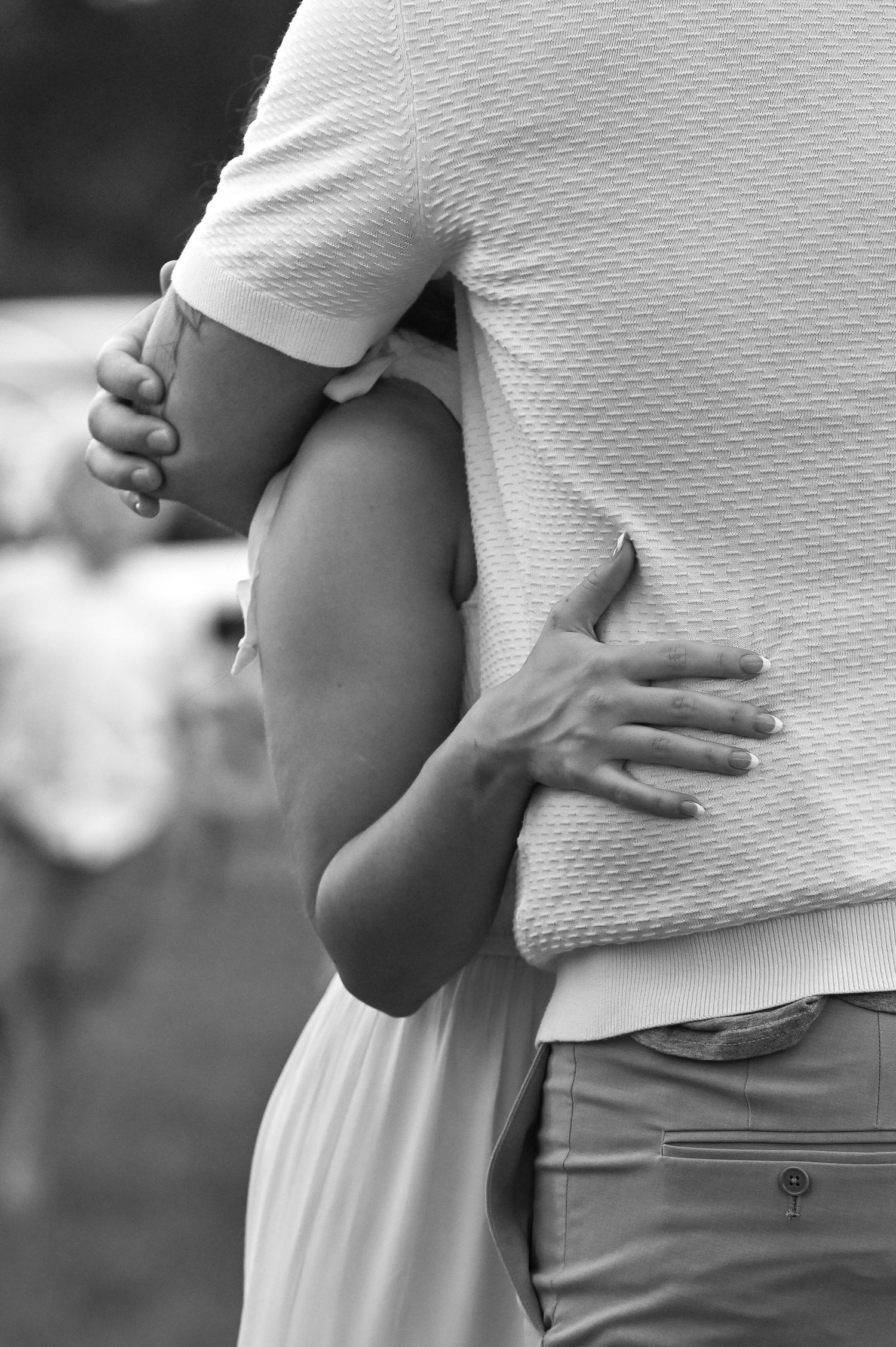 Black and white photo of a couple embracing outdoors, hands wrapped around each other in a tender hug.