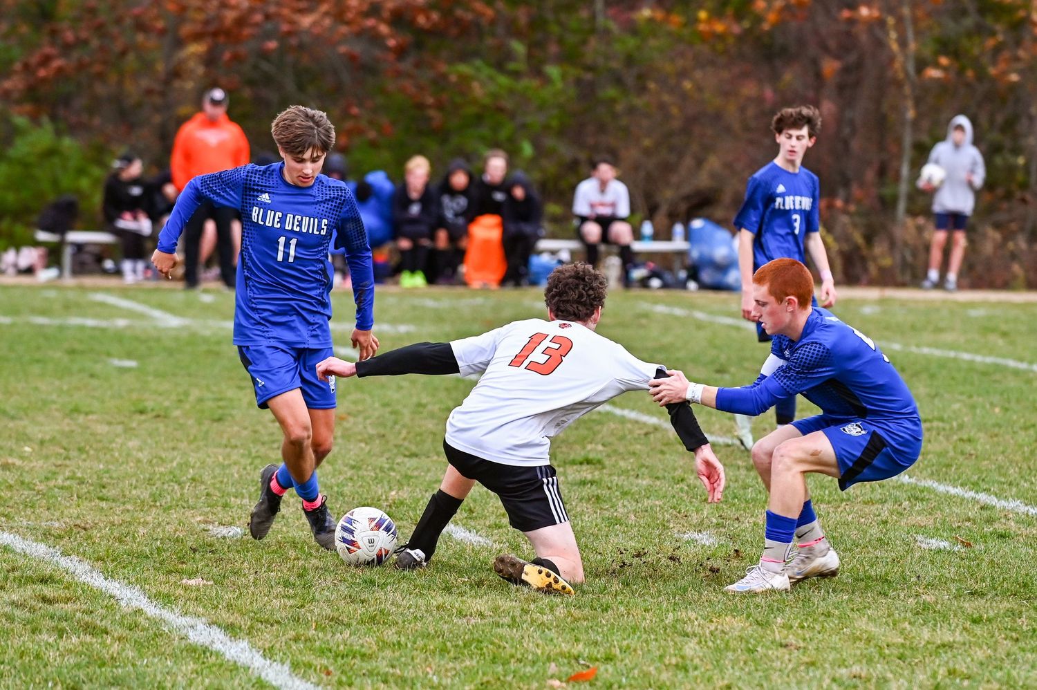 Soccer players compete for possession of the ball during an intense match on a grass field.