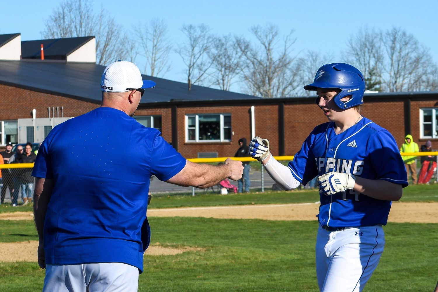 Baseball coach and player fist bump during a game on sunny spring day.