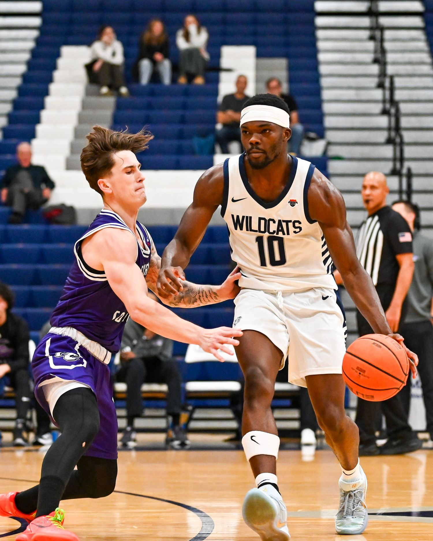 Two basketball players in action during a game, with a Wildcats player in white jersey number 10 dribbling against defender.