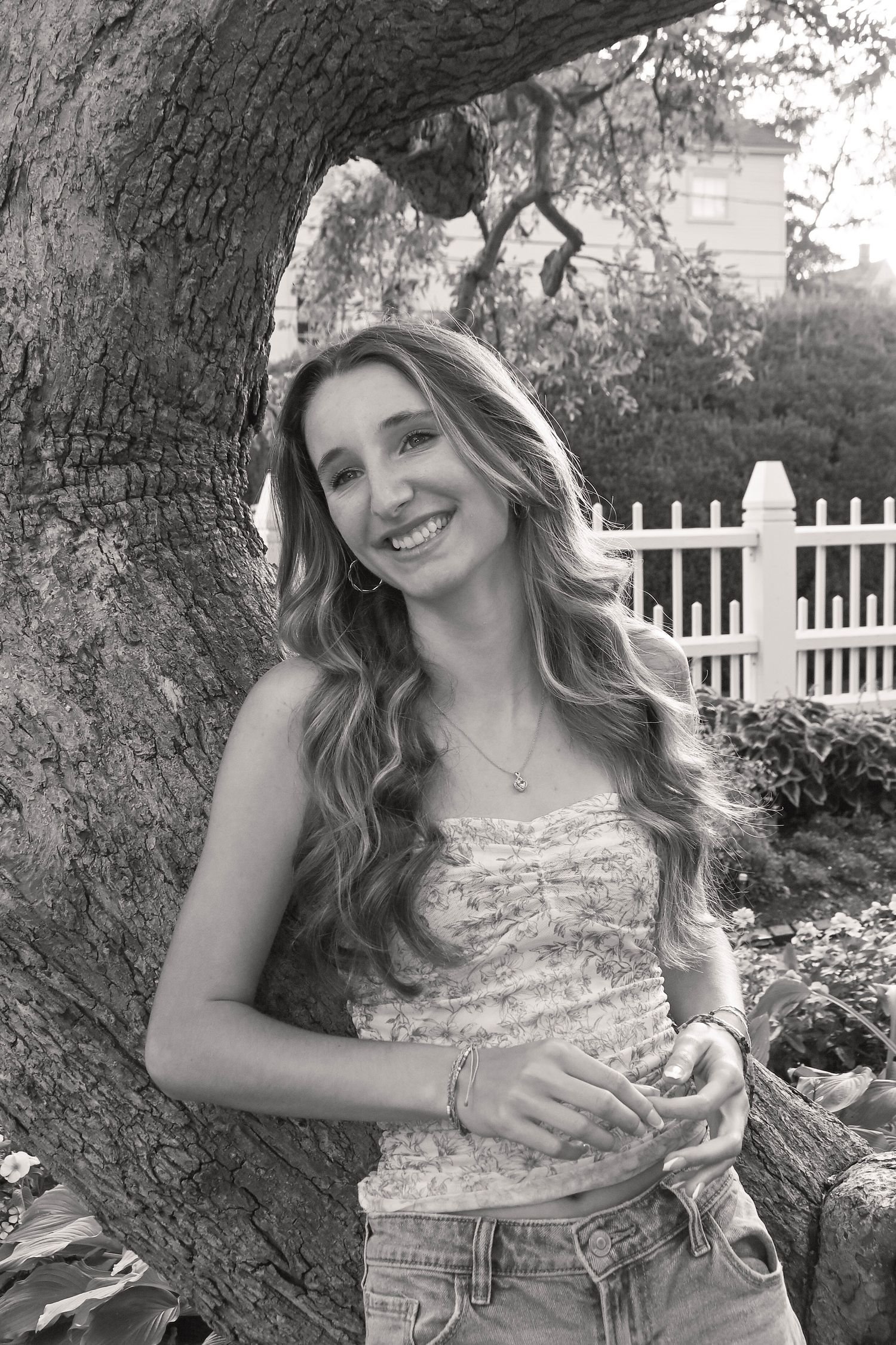 Black and white photo series showing a woman in a floral top posing playfully against a tree trunk outdoors.