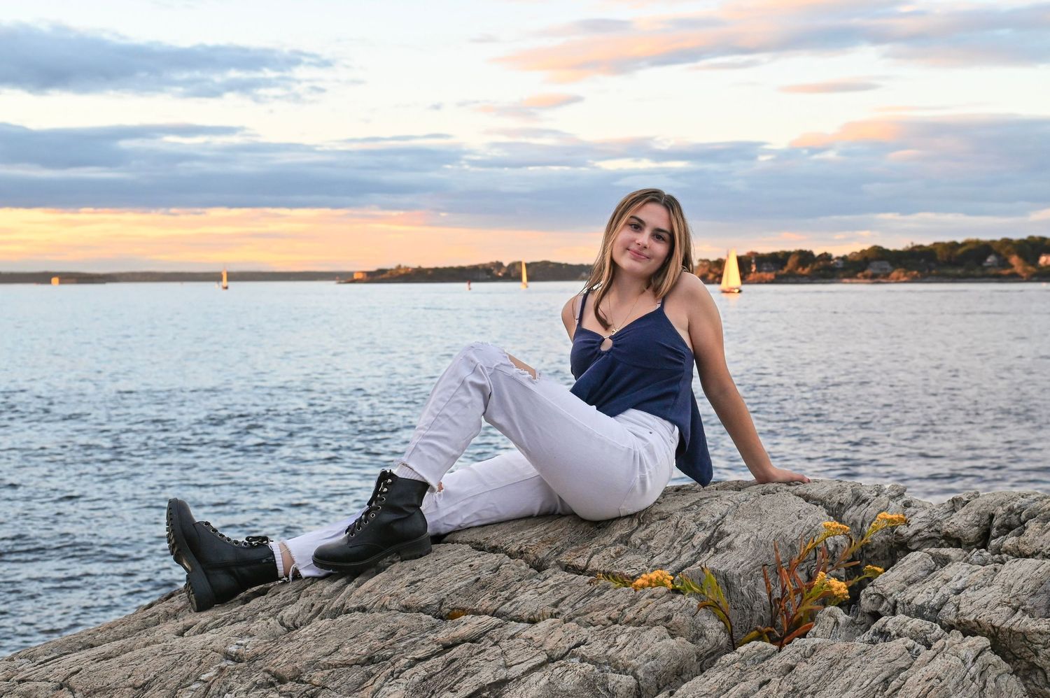 A person in white lounging on seaside rocks during sunset over a coastal shoreline.