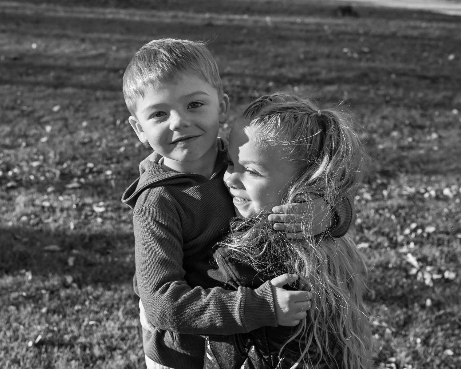 A black and white photo series shows a young child playing and interacting with a small dog outdoors.