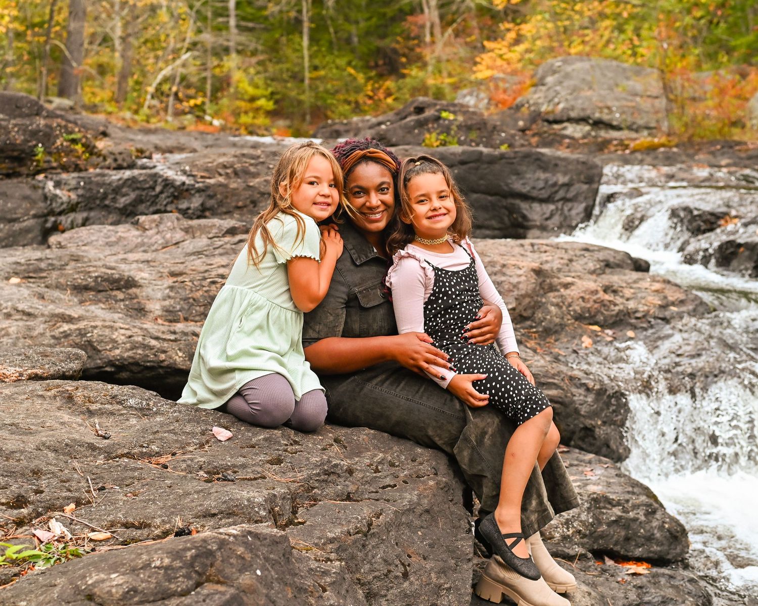 People enjoying a scenic autumn waterfall on rocky terrain during a fall foliage photoshoot.