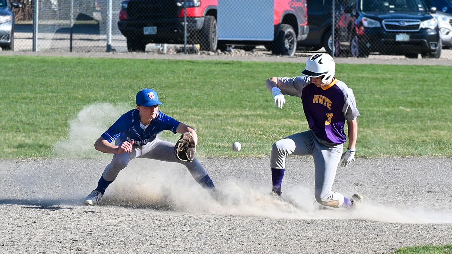 Baseball player slides into base creating dust cloud while defender prepares to make the tag during game.