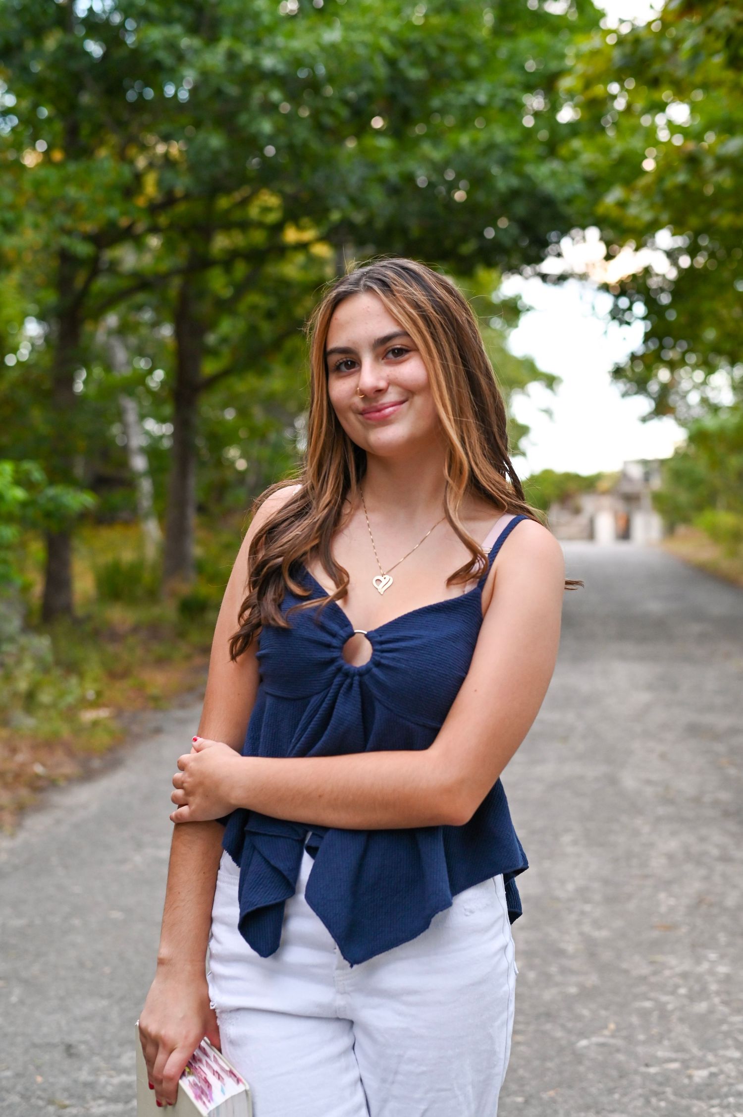 A person in a navy blue and white outfit stands on a gravel path surrounded by green trees on a sunny day.