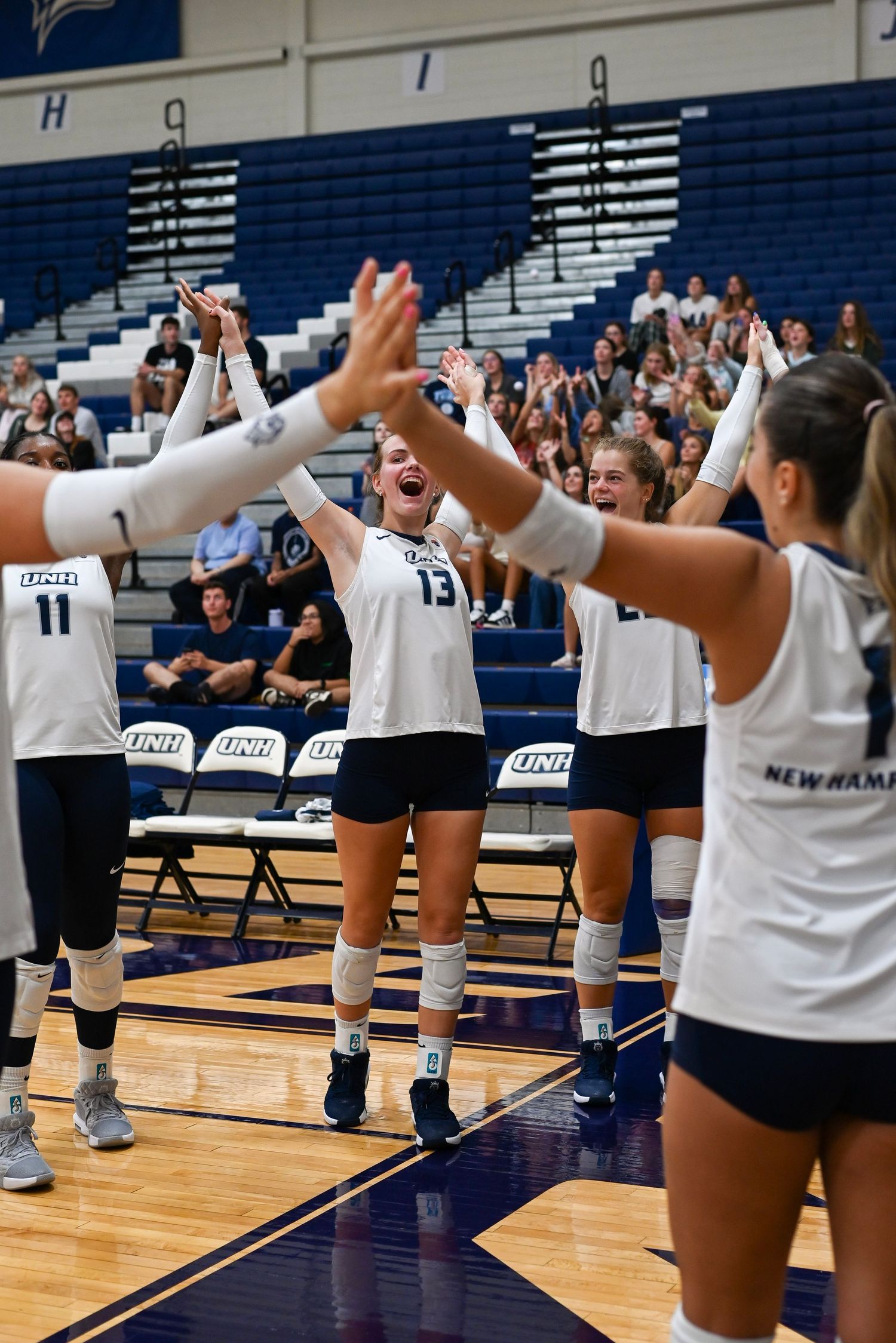 Women's volleyball team celebrates with high fives during a game in the gym at UNH's Lundholm Gymnasium.